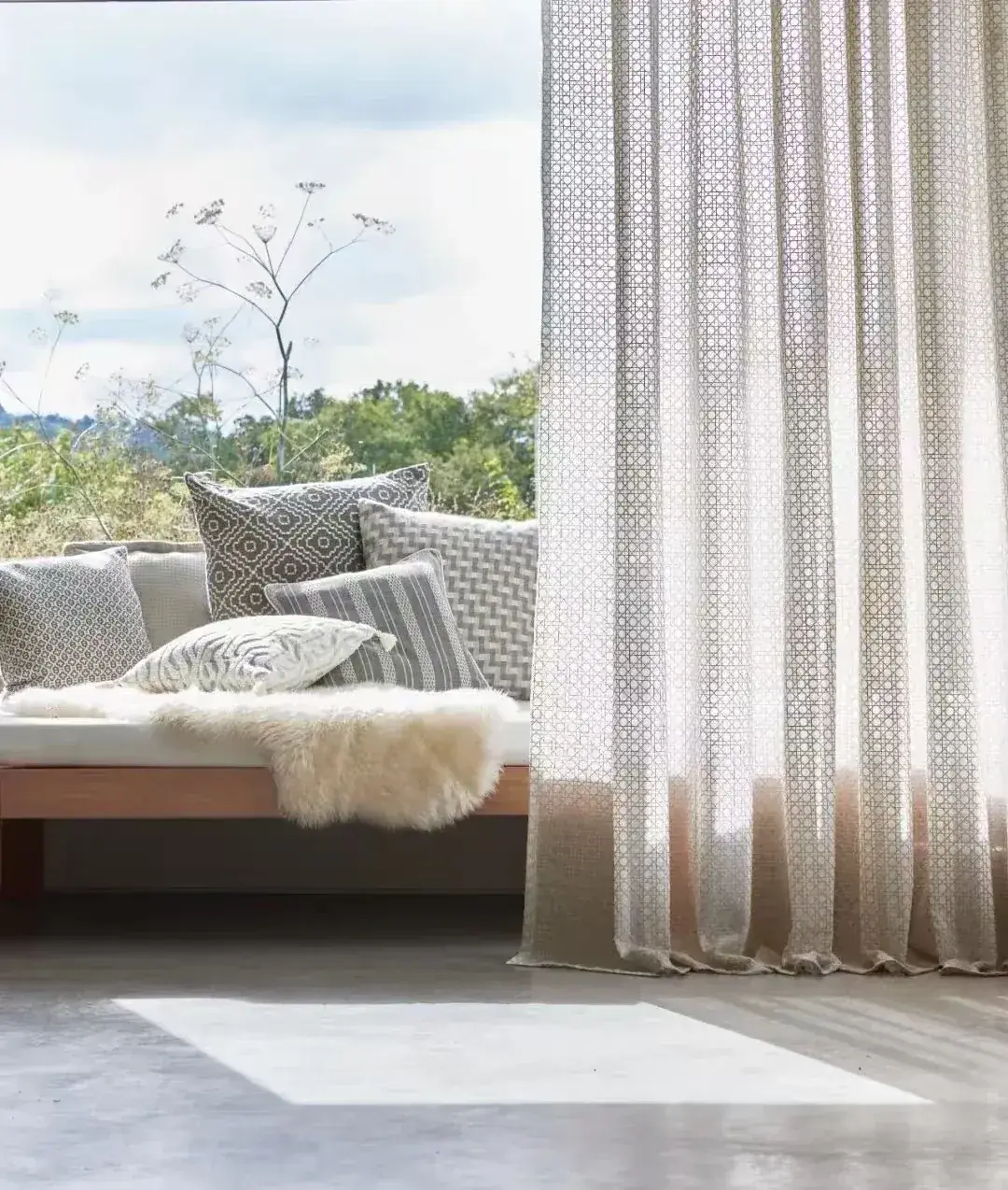 Soft sheer curtain filtering daylight beside a calm upholstered window seat