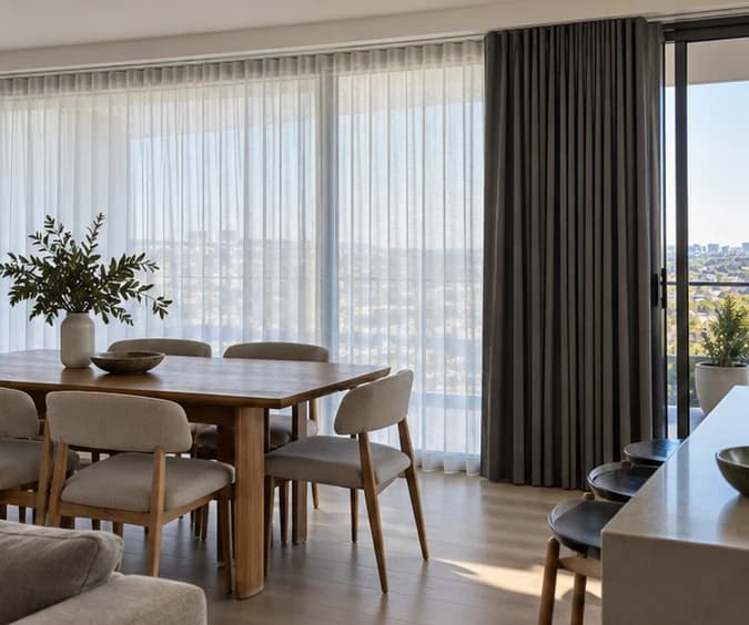 Daylight passing through a drawn sheer with a charcoal blockout layer stacked independently beside a dining area