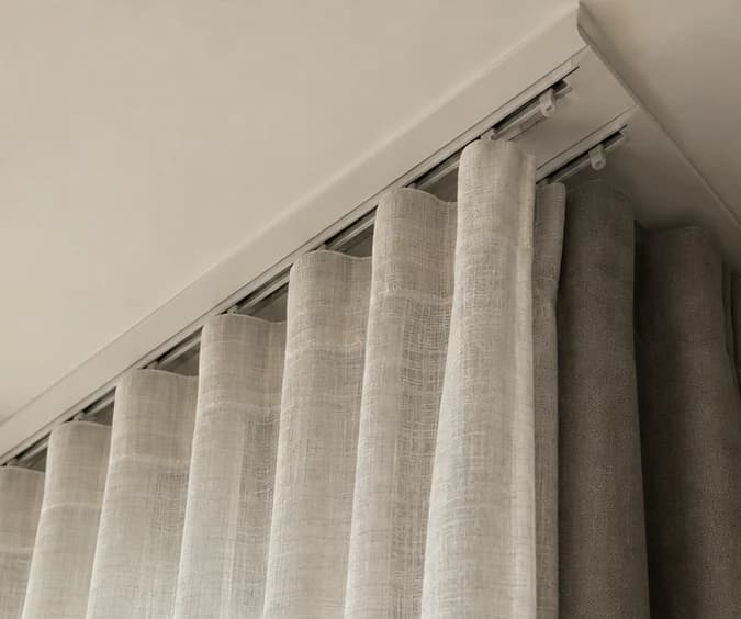 Two separate ceiling-mounted curtain tracks with visible carriers and space between sheer and lined layers