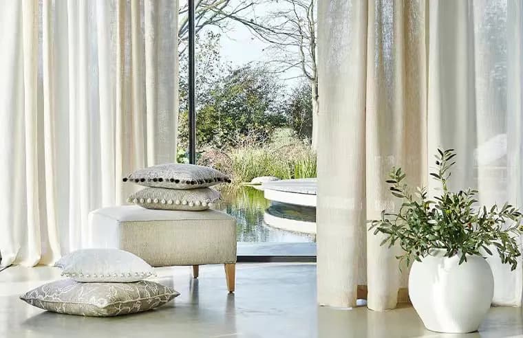 Full-height warm neutral sheer curtains surrounding a calm, light-filled living area