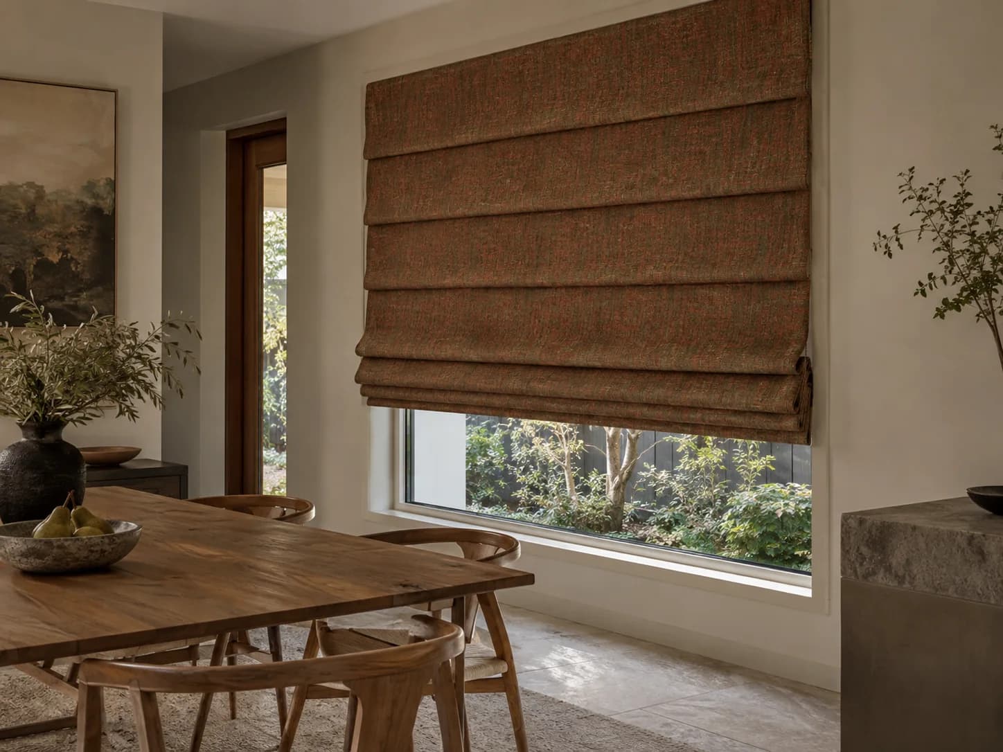 Rust-toned Waterfall Roman blind with projecting layered folds in a timber dining room